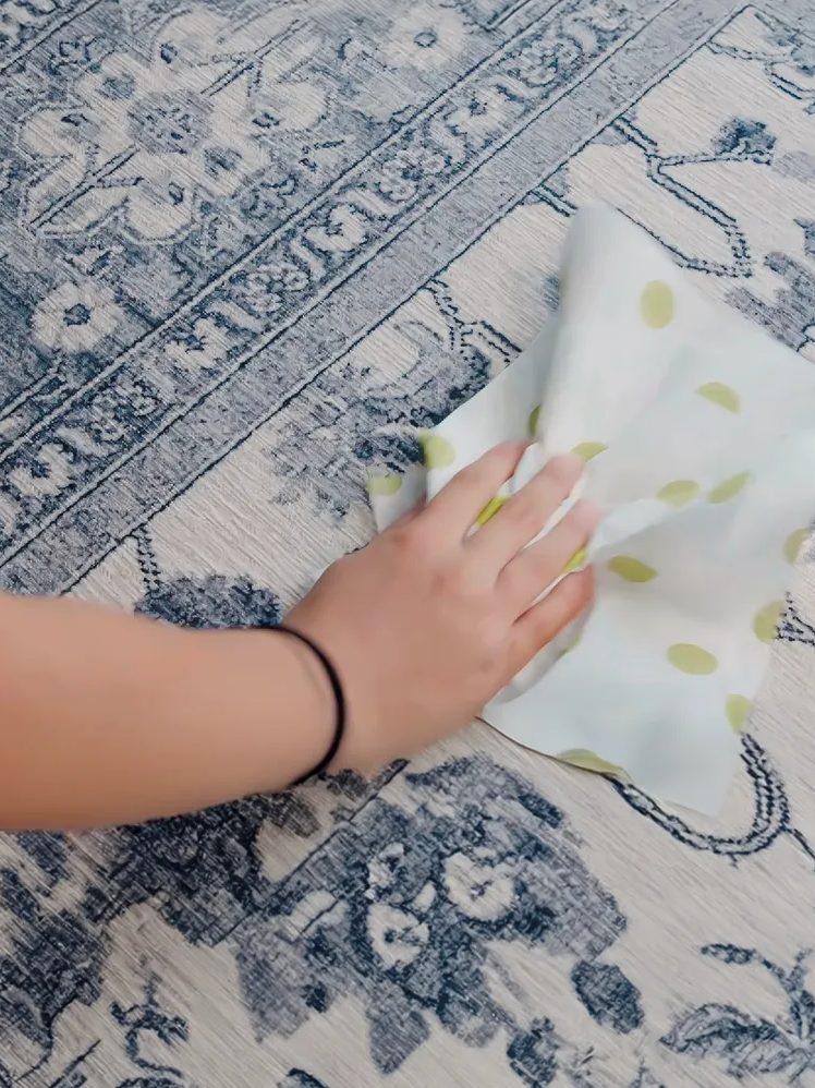 Una mano tampona una macchia sul tappeto con un panno
